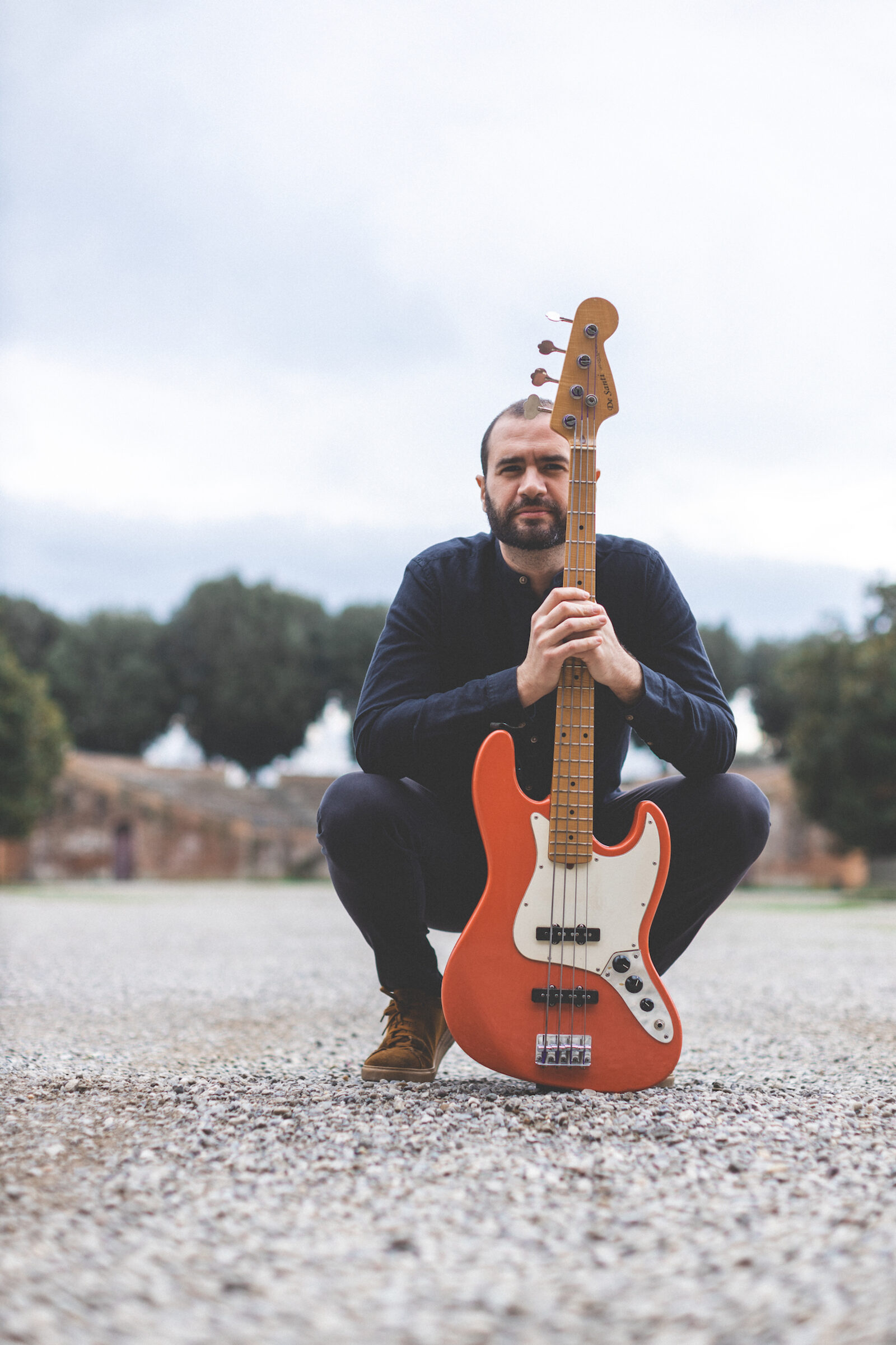 Giuseppe Vitale crouching with his electric bass under a grey sky